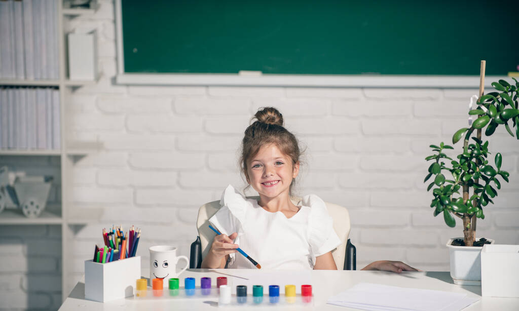Cute little girl child painting with paints color and brush. Drawing lesson in school. Kids early arts and crafts education - Foto, imagen