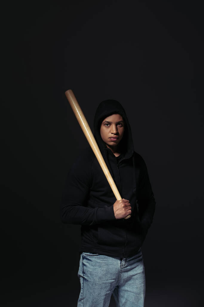 African american hooligan holding baseball bat and looking at camera isolated on black  - 写真・画像
