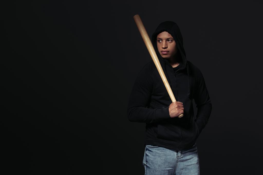Afroamerikanischer Hooligan mit Baseballschläger schaut isoliert auf schwarz  - Foto, Bild