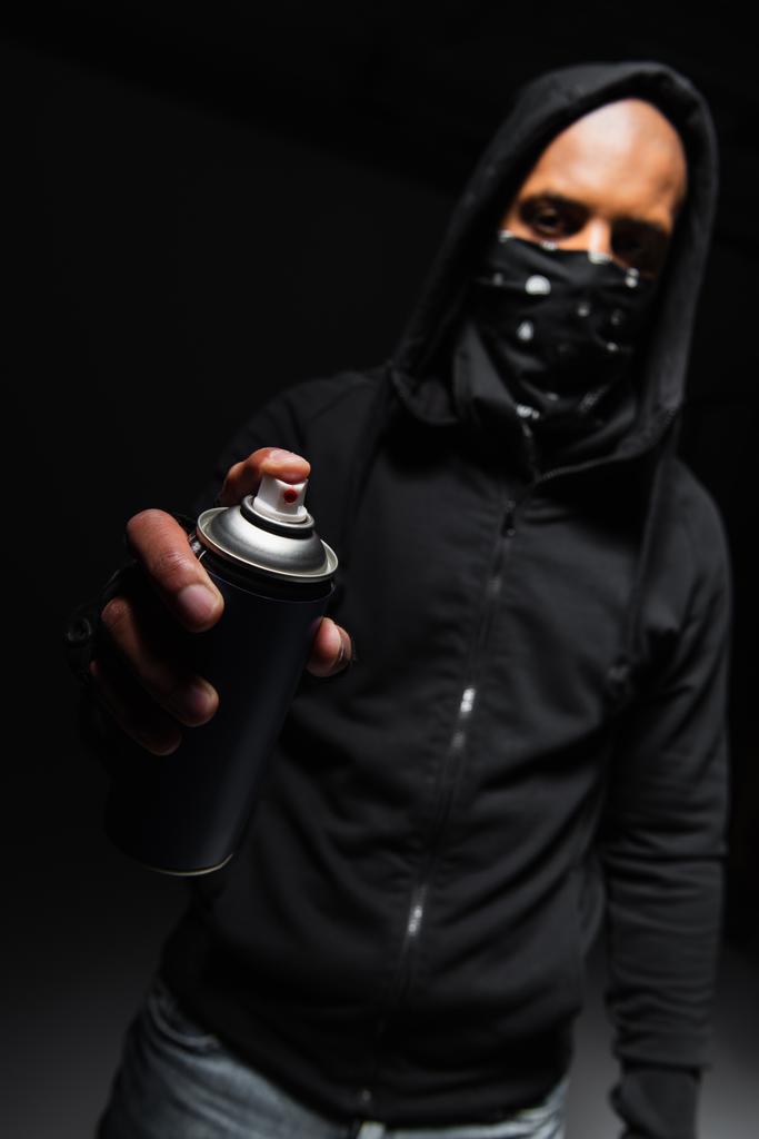 Blurred african american hooligan with mask on face holding spray paint on black background  - Foto, immagini