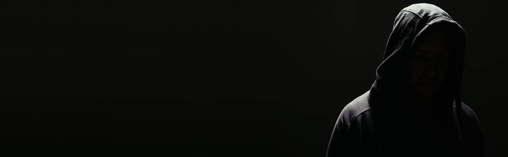 Σιλουέτα χούλιγκαν με κουκούλα με φωτισμό απομονωμένο σε μαύρο, λάβαρο  - Φωτογραφία, εικόνα
