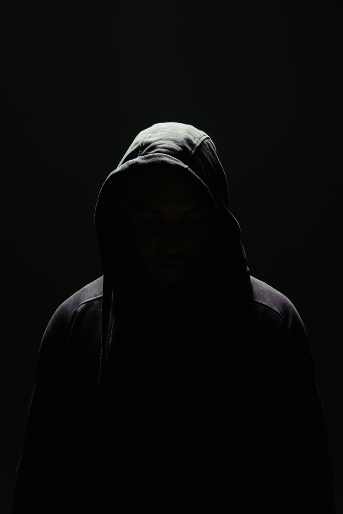 Silhouette von Hooligan mit Kapuze steht in Beleuchtung isoliert auf schwarz  - Foto, Bild