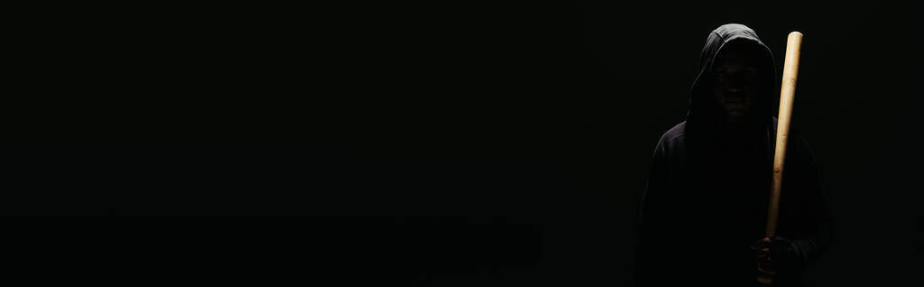 Силуэт хулигана, держащего бейсбольную биту при освещении изолирован на черном, баннер  - Фото, изображение