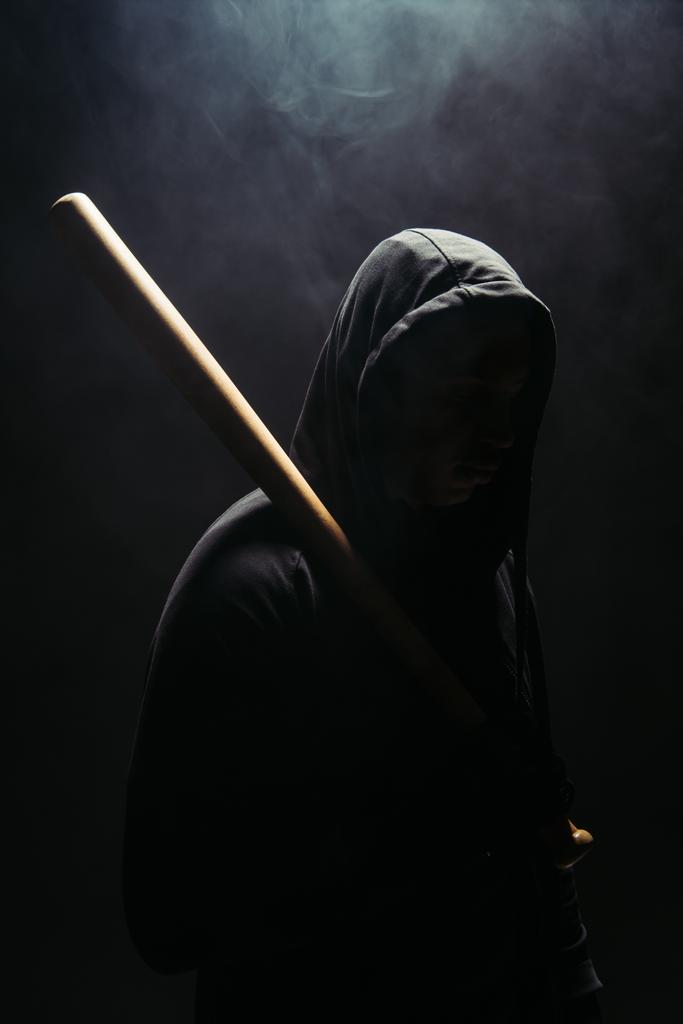 Silhouette of bandit holding baseball bat on black background with smoke  - Foto, afbeelding
