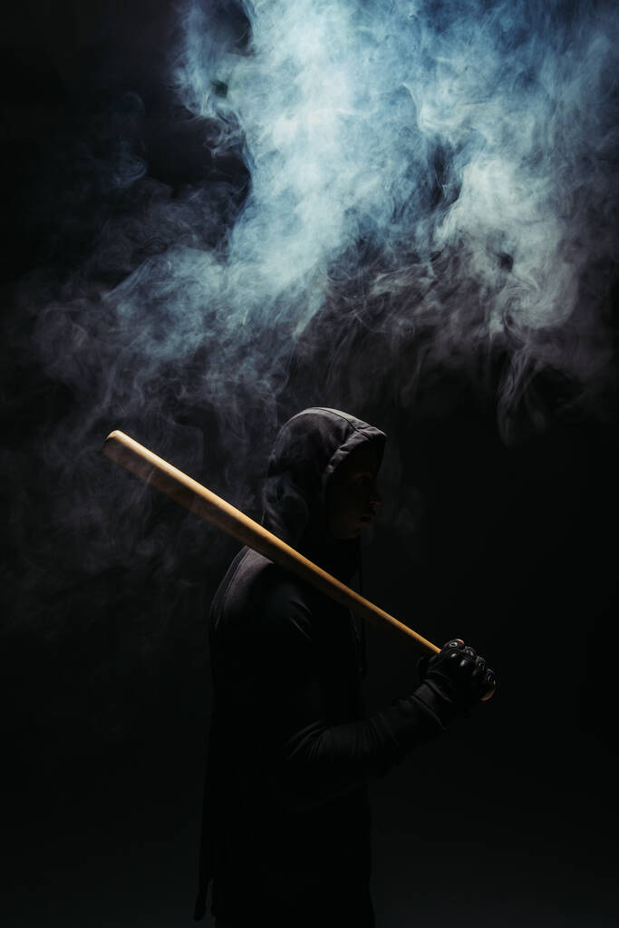 Silhouet van bandiet met houten honkbalknuppel op zwarte achtergrond met rook  - Foto, afbeelding