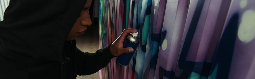 Vista lateral do vândalo afro-americano desenhando grafite na parede, bandeira   - Foto, Imagem