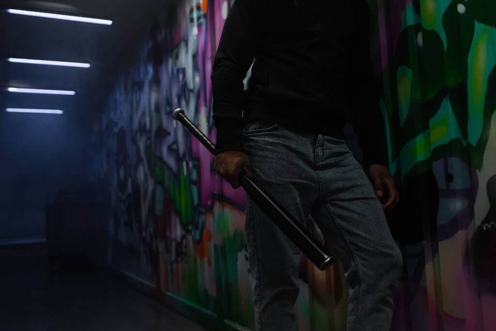 Обрізаний вид афроамериканського бандита, який тримає бейсбольну кажана біля графіті на стіні в гаражі
  - Фото, зображення