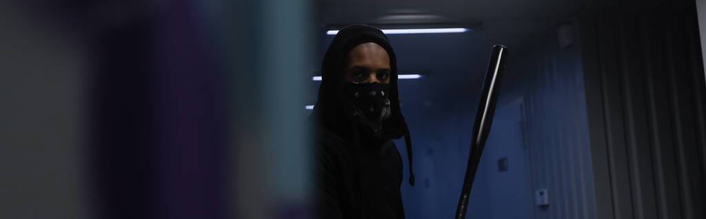 Африканский американский хулиган с маской на лице с бейсбольной битой в гараже, баннер  - Фото, изображение