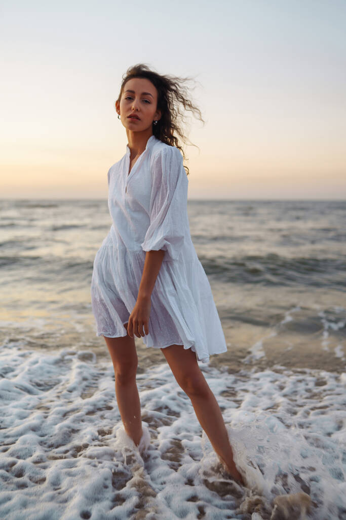Deniz kenarında poz veren zarif beyaz elbiseli şık bir kadın. İnsanlar, özgürlük, yaşam tarzı, seyahat ve tatil kavramı. - Fotoğraf, Görsel