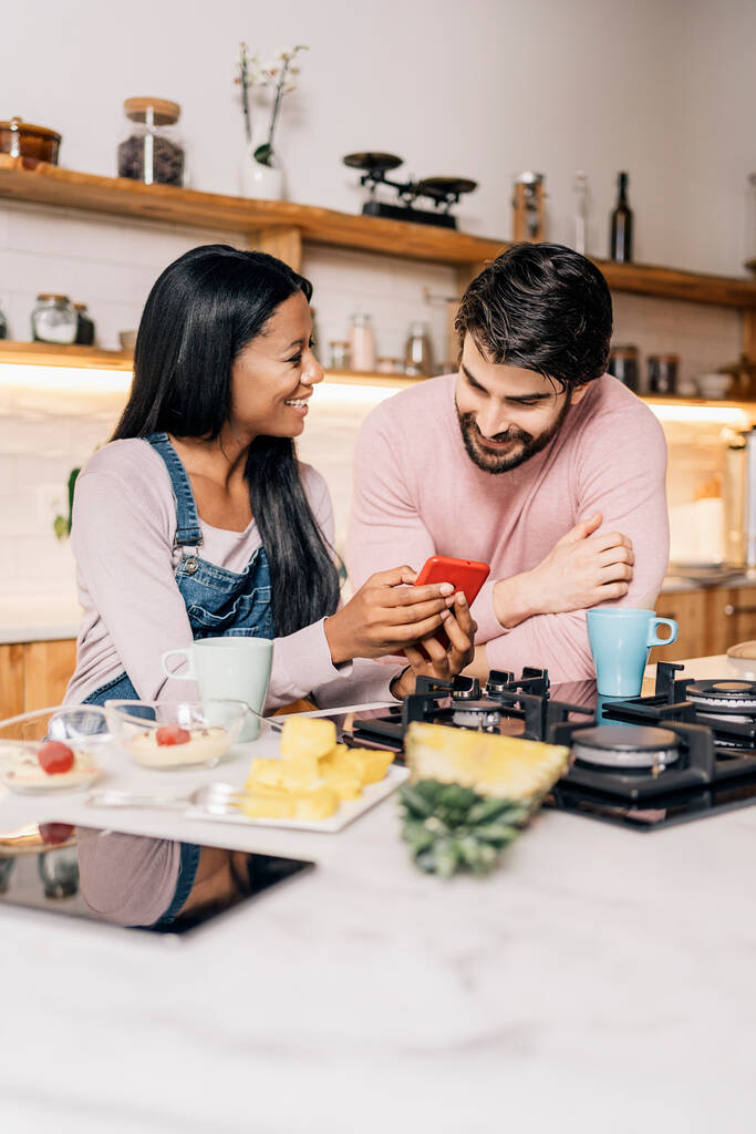 Счастливая пара завтракает на кухне дома и пользуется телефоном. - Фото, изображение