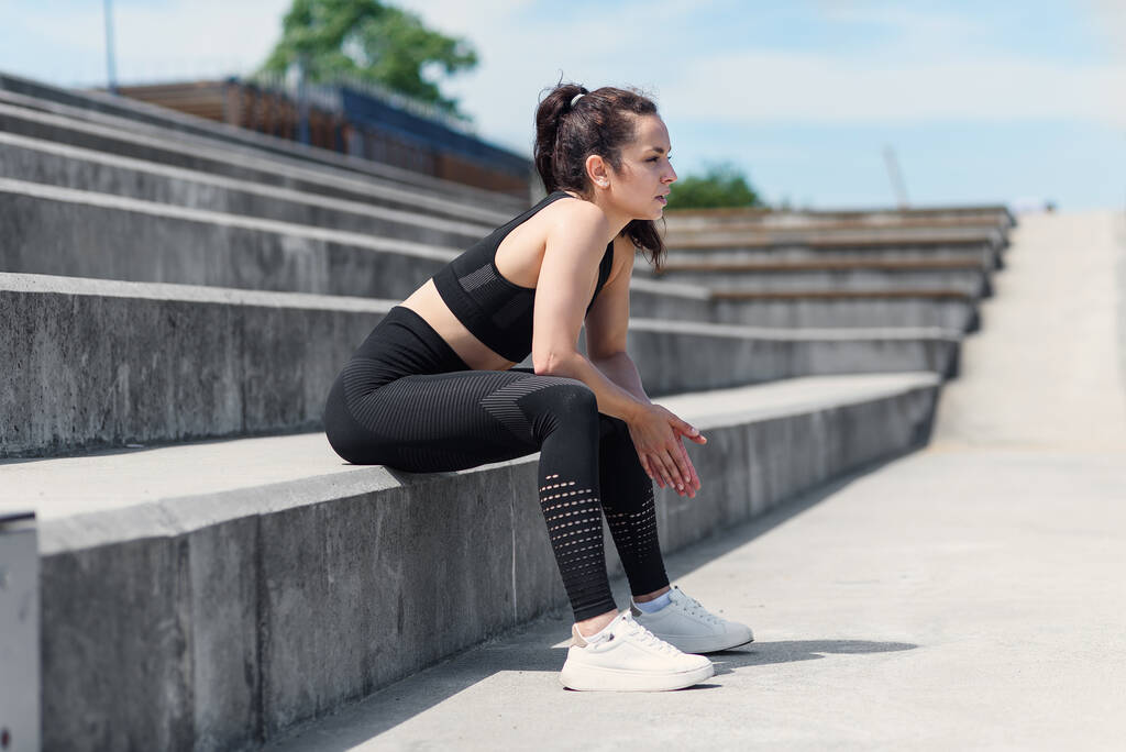Exhausted pretty woman after hard outdoor training sitting on stairs at sports stadium. Healthy active lifestyle concept. - Foto, Imagen