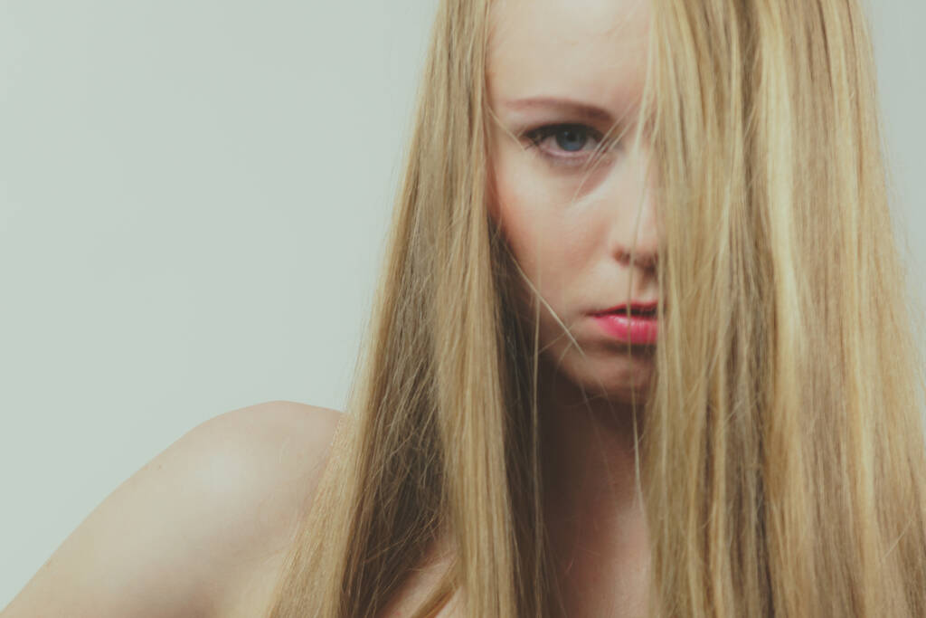 Smutna młoda kobieta zakrywa twarz długimi blond włosami. - Zdjęcie, obraz