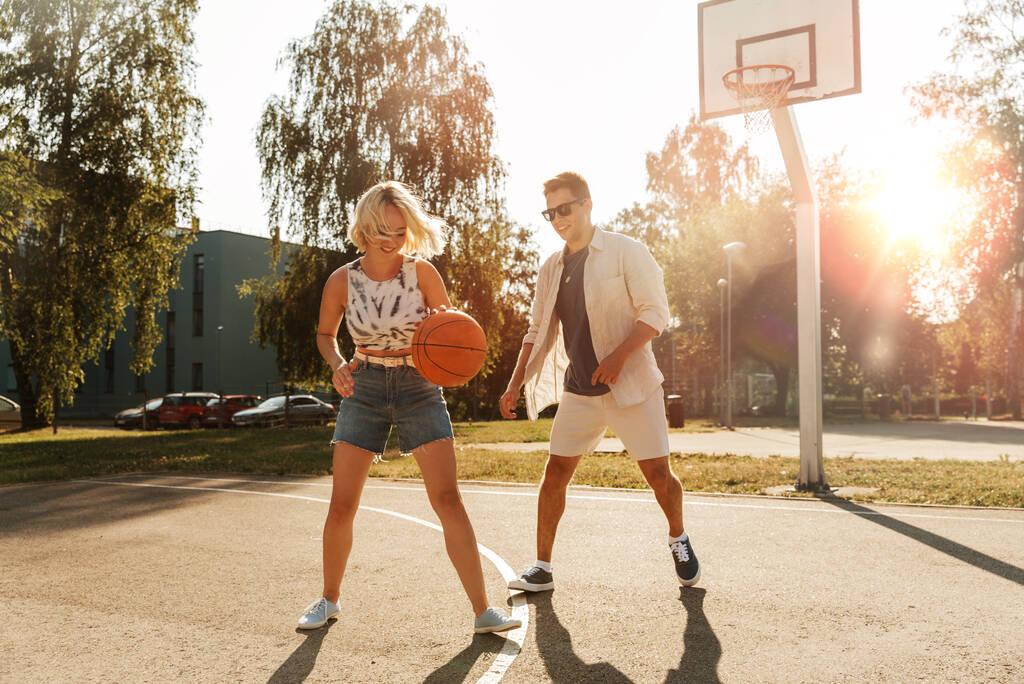 vacanze estive, sport e concetto di persone - felice giovane coppia con palla che gioca sul campo da basket - Foto, immagini