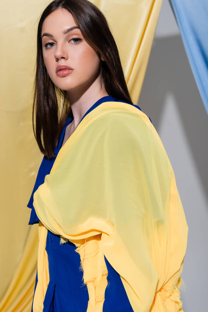 junge Ukrainerin in Farbblockkleidung posiert in der Nähe blauer und gelber Vorhänge  - Foto, Bild