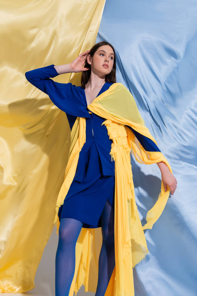 брюнетка молода українка в барвистому одязі, поставленому біля синіх і жовтих завіс.  - Фото, зображення