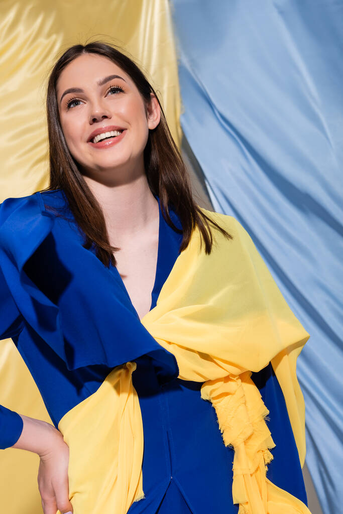 positive ukrainian woman in color block clothing posing near blue and yellow flag - Foto, afbeelding