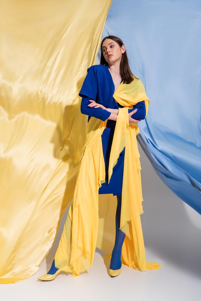 teljes hossza magabiztos ukrán nő divatos színes blokk ruházat pózol közelében kék és sárga szövet - Fotó, kép
