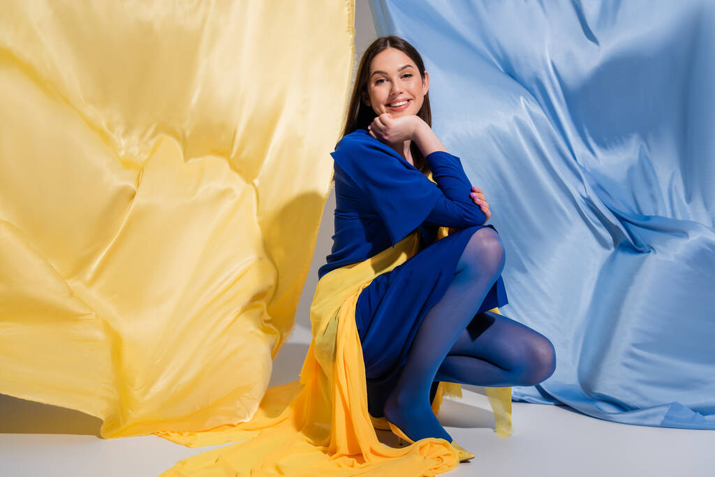 boldog ukrán nő elegáns színes blokk ruházat ül közel kék és sárga szövet - Fotó, kép