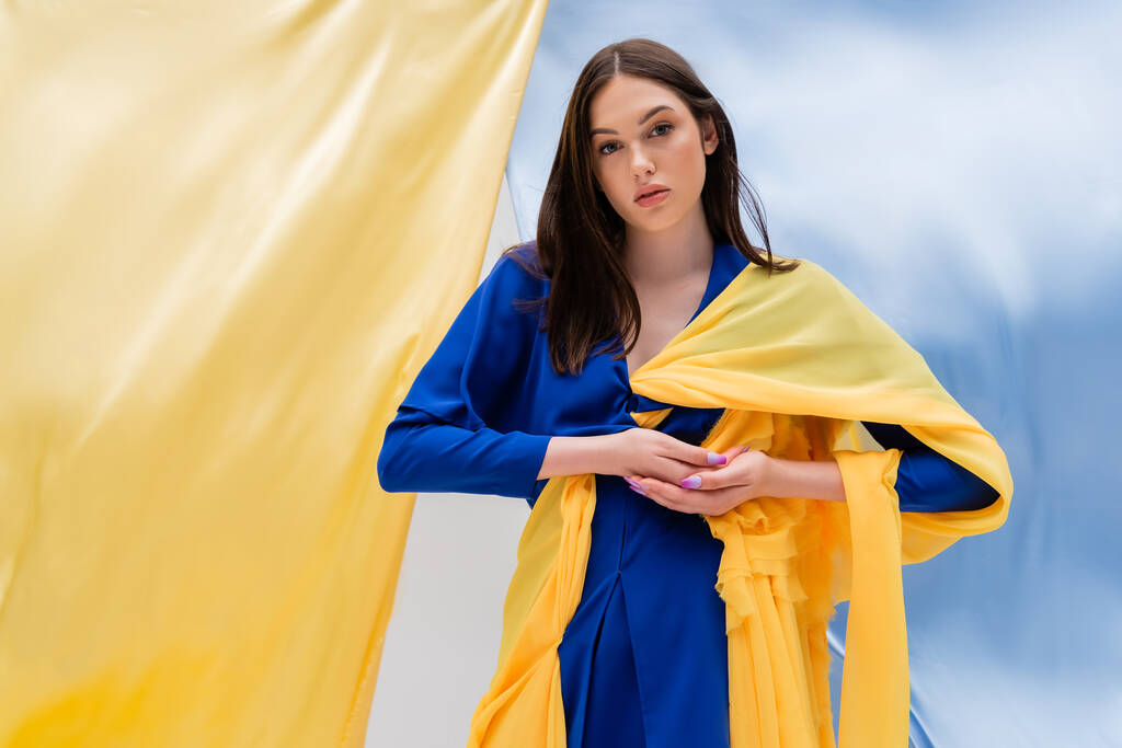 patriotic ukrainian young woman in stylish clothing posing near blue and yellow fabric - Photo, Image