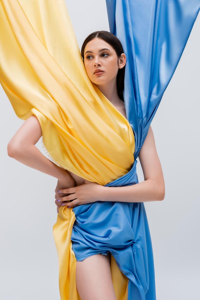 young ukrainian woman in blue and yellow dress posing with hand on hip isolated on grey - Foto, Imagem