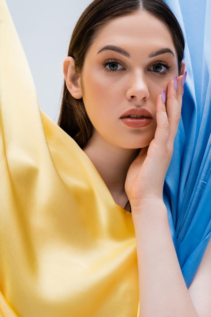 portrait of pretty and young ukrainian woman near blue and yellow fabric isolated on grey - 写真・画像
