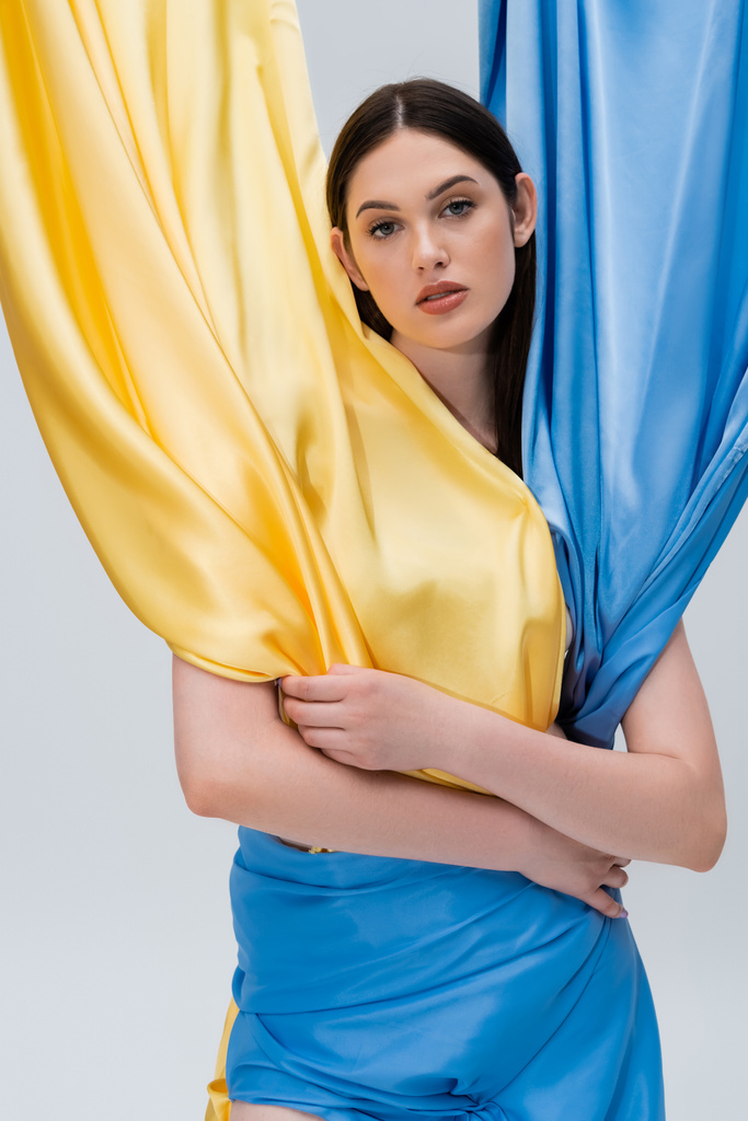 чувственная молодая украинка в синем и желтом платье позирует изолированно на сером - Фото, изображение