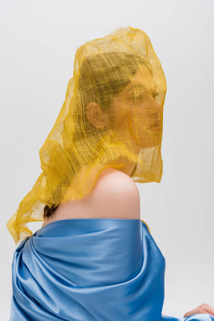 young ukrainian woman woman with yellow drapery covering face looking away isolated on grey - Photo, Image
