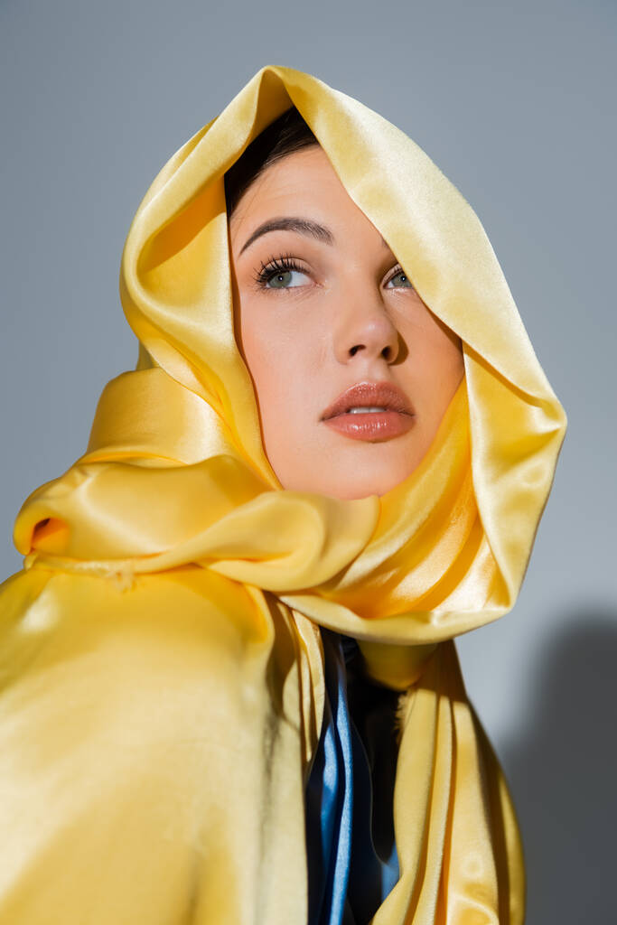 pretty ukrainian woman in yellow silk headscarf looking away isolated on grey - Fotó, kép