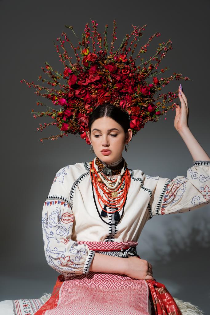 portrait of young ukrainian woman in traditional clothing and floral red wreath on grey - Foto, immagini