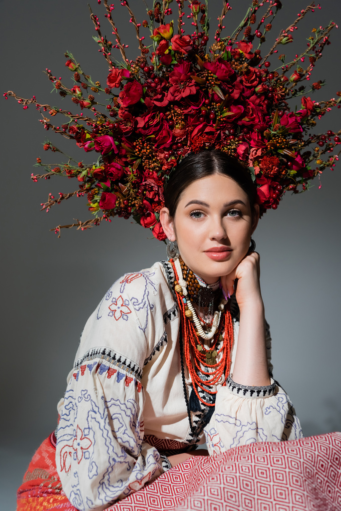 portrait of young ukrainian woman in traditional costume and floral red wreath isolated on grey - Foto, immagini