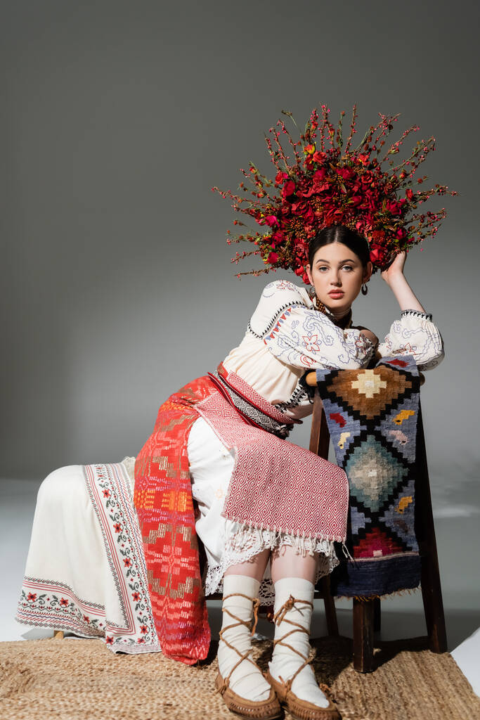 full length of pretty ukrainian woman in traditional dress and red wreath with flowers and berries on grey - 写真・画像