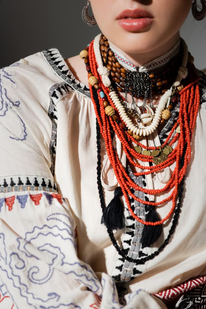 częściowy widok ukraińskiej kobiety w tradycyjnych ubraniach i kwiatowy czerwony wieniec izolowany na szarości - Zdjęcie, obraz