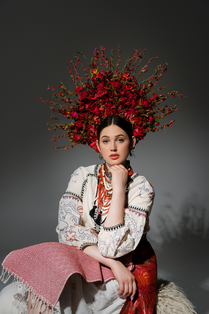 pretty ukrainian woman in traditional clothes and red wreath with flowers and berries on grey - Foto, Imagen