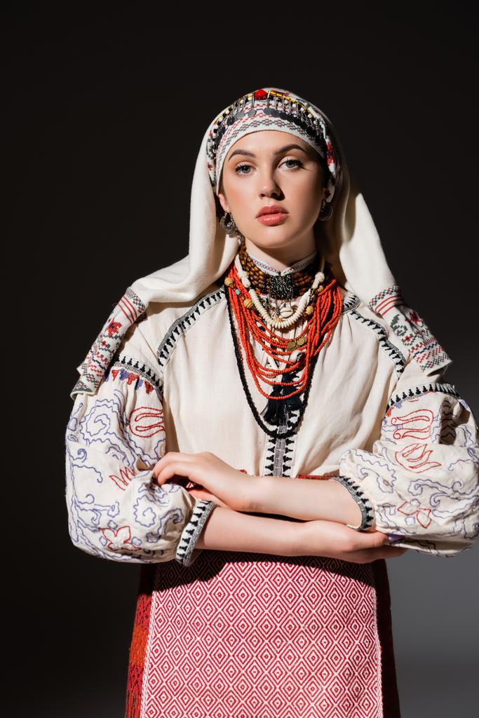 young ukrainian woman in traditional shirt with ornament and red beads posing on black - Foto, Imagem
