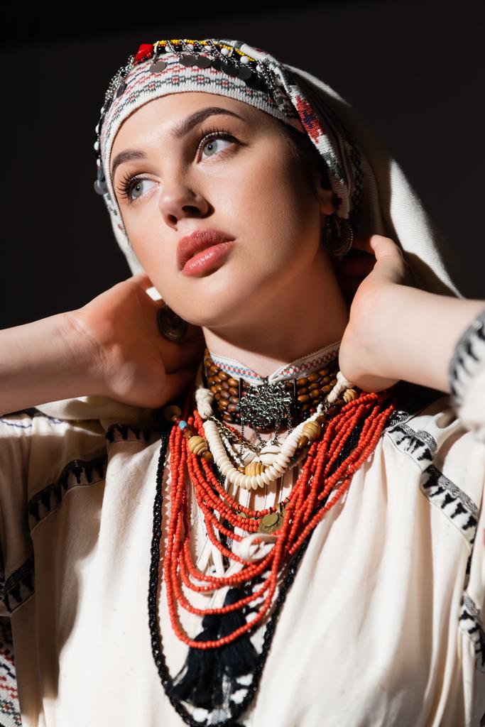 portrait of ukrainian woman in traditional shirt with red ornament and headwear posing isolated on black - Photo, Image