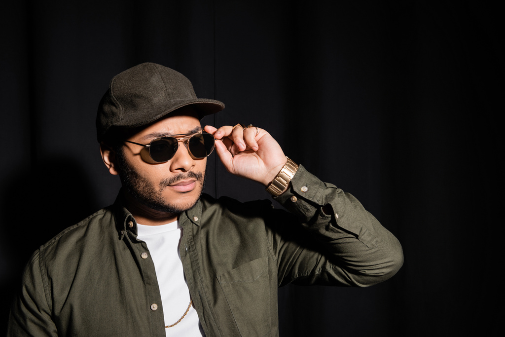 eastern hip hop performer in cap adjusting sunglasses on black - Photo, Image