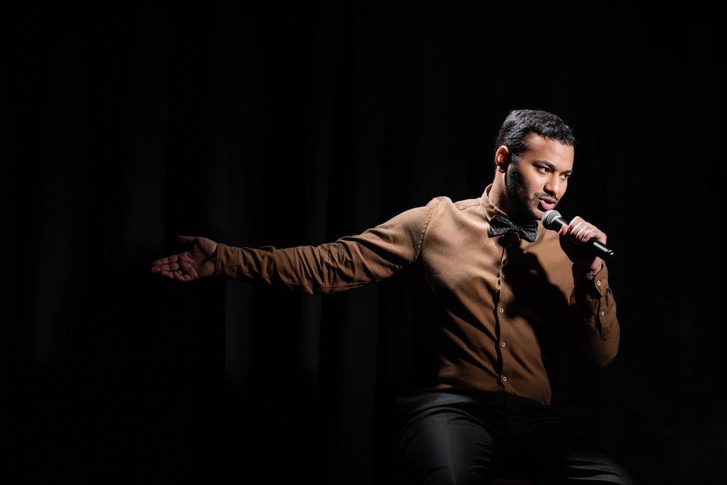 comediante oriental sentado y la realización de stand up comedia en el micrófono en negro  - Foto, imagen