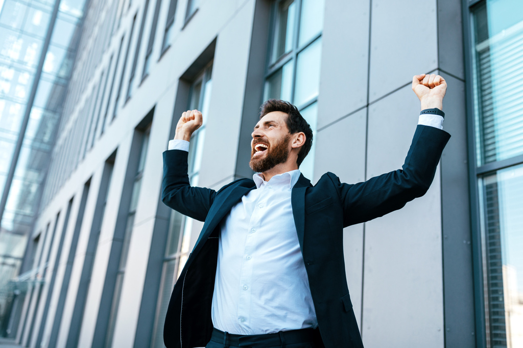 Happy satisfied excited european millennial bearded businessman in suit rejoices in successful deal or win, rises hands up near modern office building, outdoor. Manager, emotions of victory, gestures - Zdjęcie, obraz