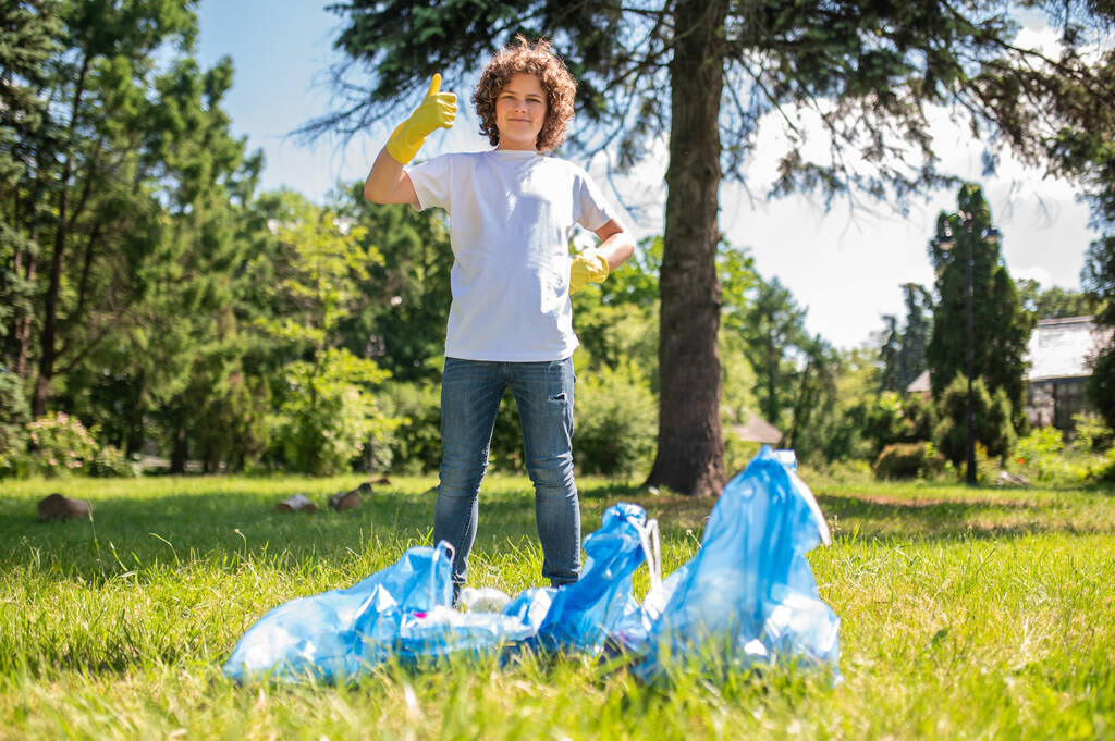 Молодцы. Уверенный подросток, стоящий рядом с сумками, полными мусора - Фото, изображение