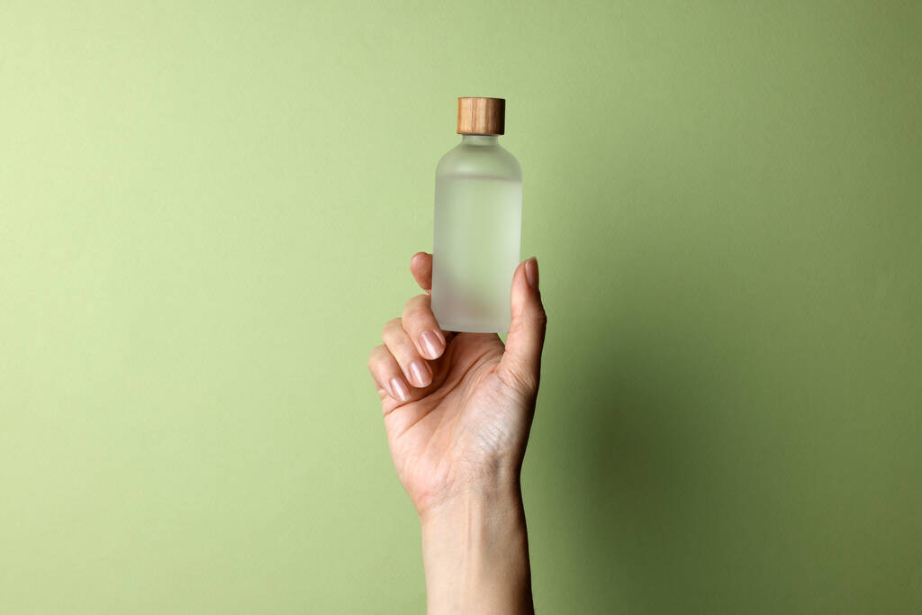 Kobieta trzymająca butelkę produktu kosmetycznego na bladym tle oliwnym, zbliżenie. Miejsce na tekst - Zdjęcie, obraz