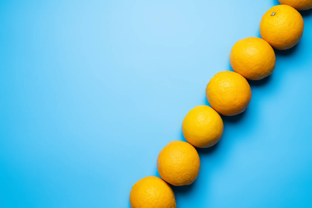 Top view of row of oranges on blue background with copy space - Foto, Imagen