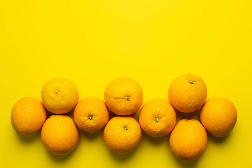Colocación plana con naranjas orgánicas con sombra sobre fondo amarillo  - Foto, imagen