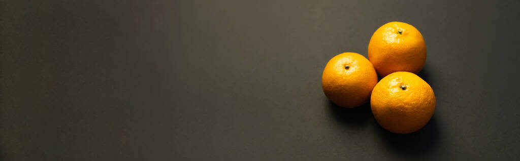 Hochwinkelaufnahme von schmackhaften Mandarinen auf schwarzer Oberfläche, Banner  - Foto, Bild