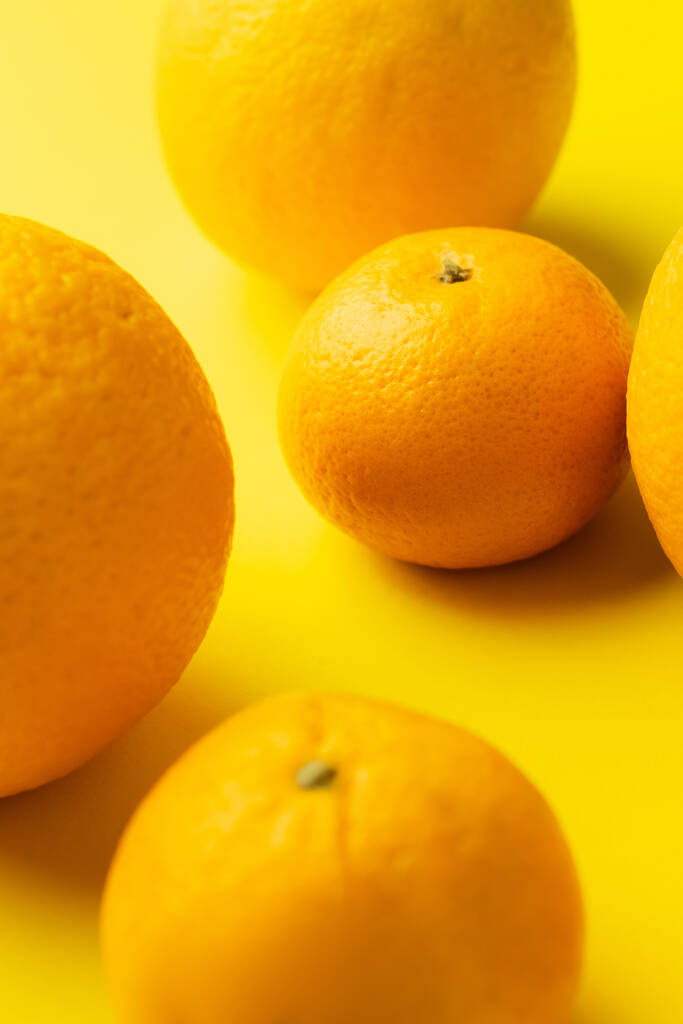 Κοντινή προβολή φρέσκων μανταρινιών και πορτοκαλιών σε κίτρινο φόντο - Φωτογραφία, εικόνα