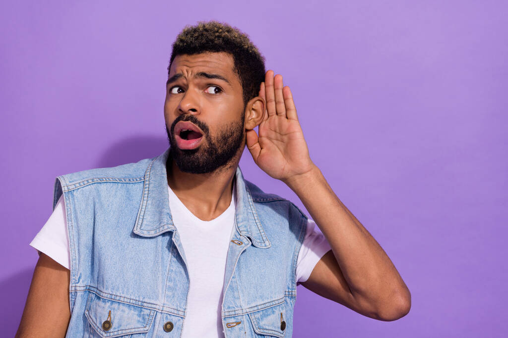 Photo of shocked funny man wear jeans waistcoat arm ear listening empty space isolated violet color background. - Fotó, kép