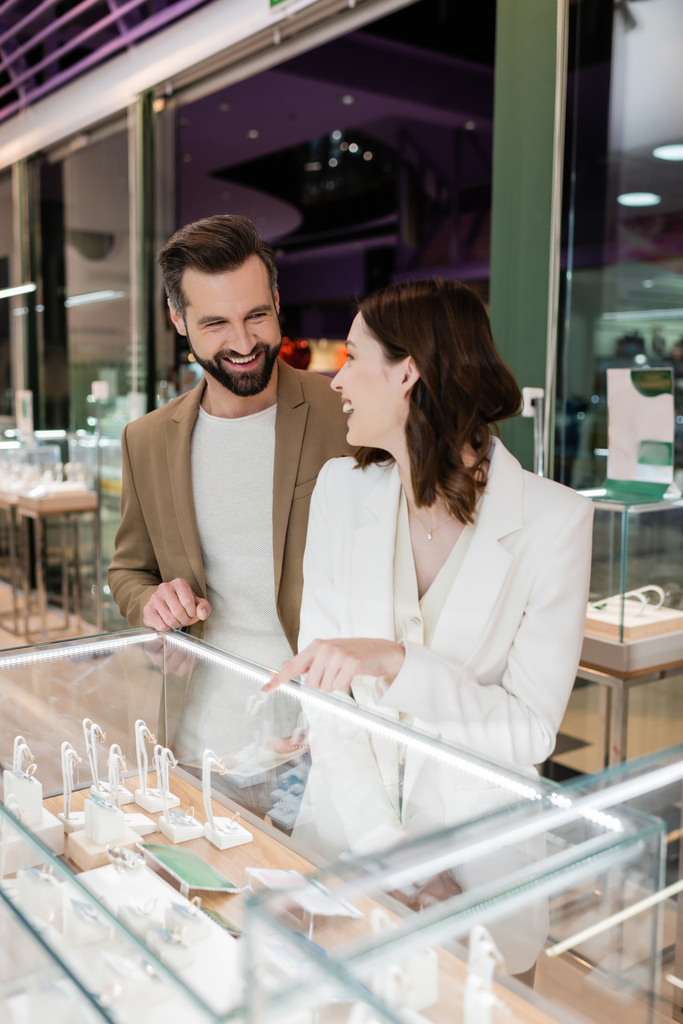 Cheerful woman pointing with finger at showcase and looking at boyfriend in jewelry shop  - Fotoğraf, Görsel
