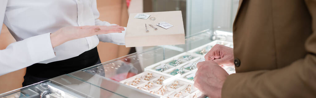 Gesneden weergave van verkoper wijzen op accessoires in de buurt van de klant in juwelier, banner  - Foto, afbeelding