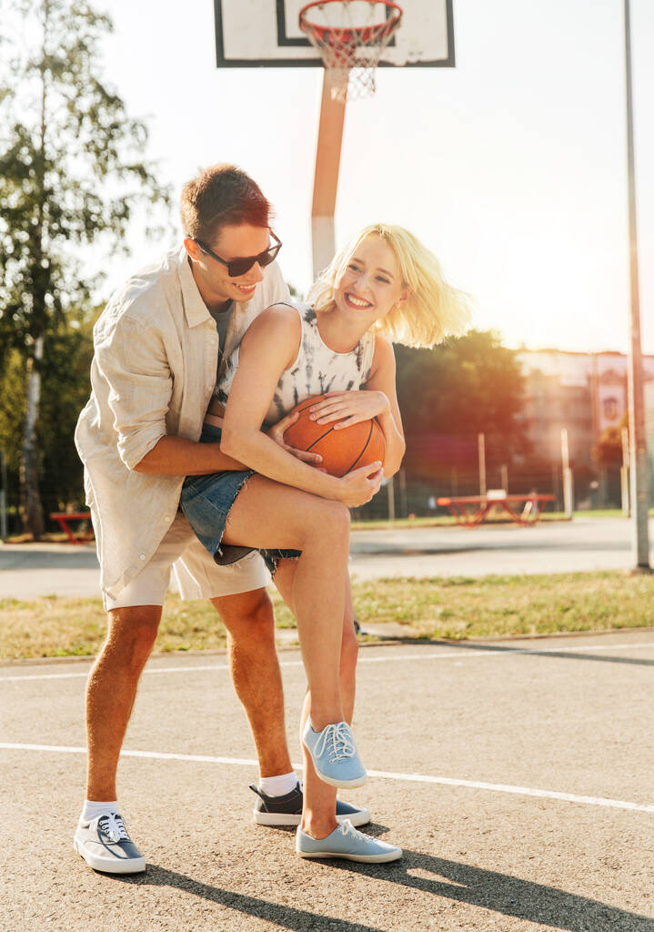 summer holidays, sport and people concept - happy young couple with ball playing on basketball playground - Photo, Image