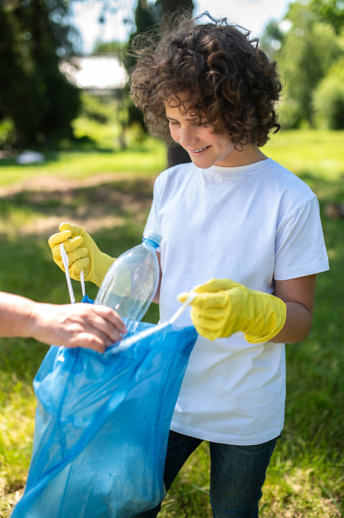 Müll. Jemand hilft einem lockigen Teenager beim Müllsammeln - Foto, Bild