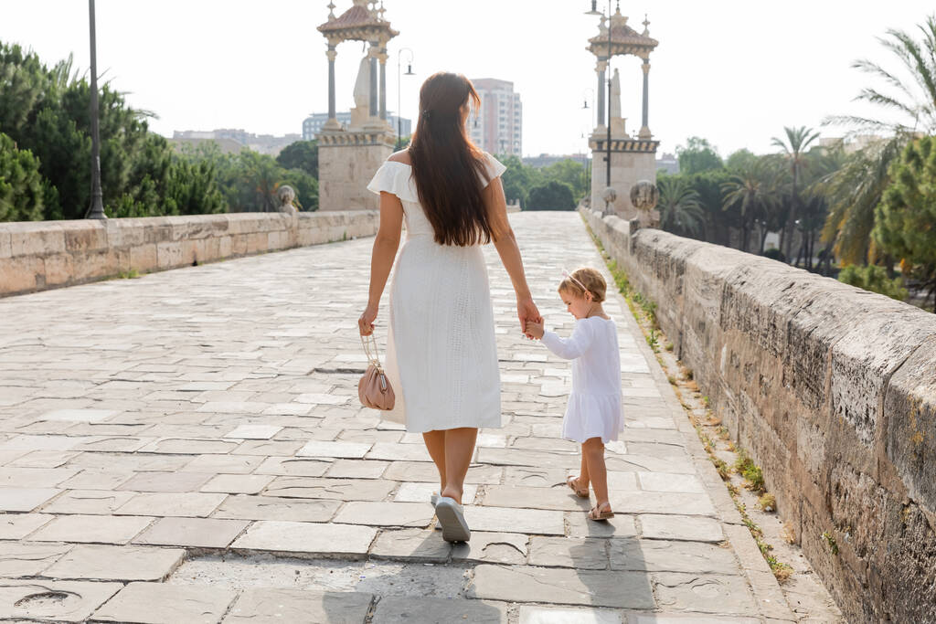Donna in abito che tiene per mano la figlia del bambino mentre cammina sul ponte Puente Del Mar a Valencia - Foto, immagini
